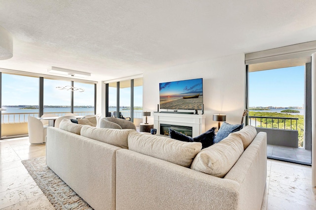 living room featuring a glass covered fireplace, floor to ceiling windows, a water view, and a textured ceiling