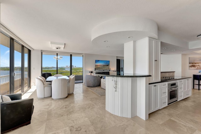 kitchen featuring dark stone countertops, oven, floor to ceiling windows, white cabinetry, and open floor plan