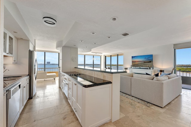 kitchen with visible vents, a kitchen island with sink, dark countertops, white cabinetry, and appliances with stainless steel finishes