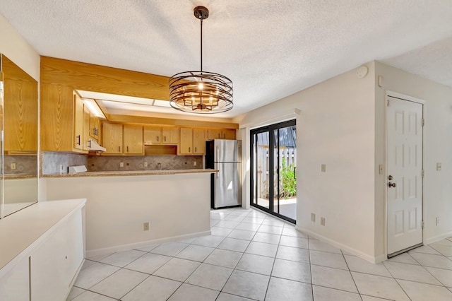 kitchen with light tile patterned floors, a peninsula, freestanding refrigerator, decorative backsplash, and under cabinet range hood