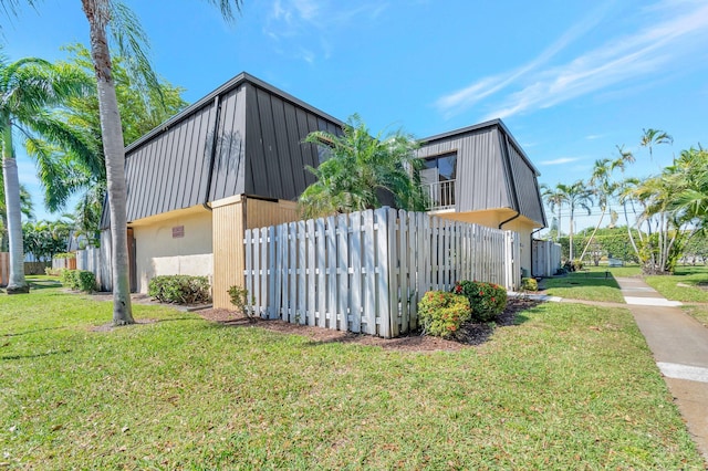 view of home's exterior with metal roof, mansard roof, a lawn, and fence