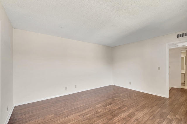 spare room with visible vents, baseboards, a textured ceiling, and dark wood finished floors