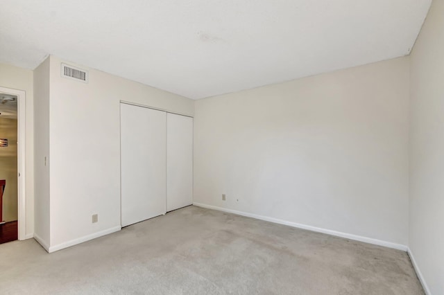 unfurnished bedroom featuring light colored carpet, visible vents, a closet, and baseboards