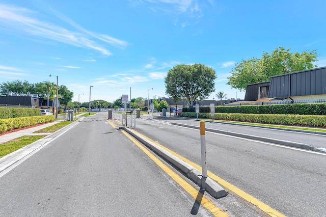 view of road featuring street lights, curbs, sidewalks, and a gated entry