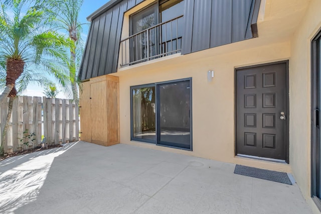 property entrance featuring stucco siding, mansard roof, a patio, and fence