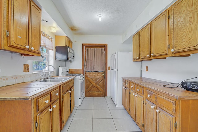 kitchen featuring a sink, a textured ceiling, white appliances, light tile patterned floors, and tile counters