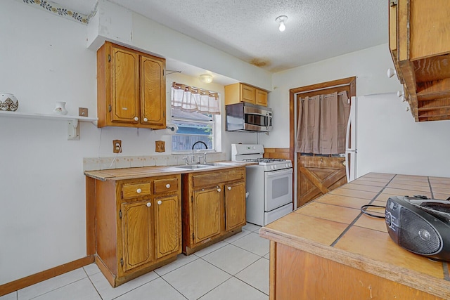 kitchen with a sink, white appliances, a textured ceiling, and brown cabinetry