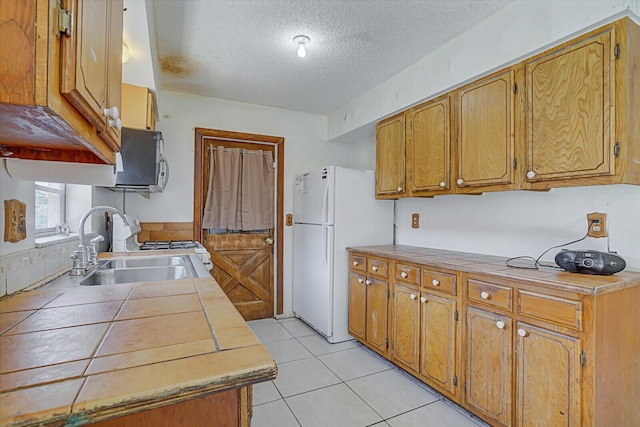 kitchen featuring tile countertops, light tile patterned floors, white appliances, a textured ceiling, and a sink