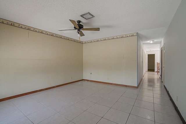 empty room with visible vents, a textured ceiling, light tile patterned floors, baseboards, and ceiling fan