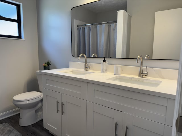 bathroom with a textured ceiling, toilet, wood finished floors, and a sink