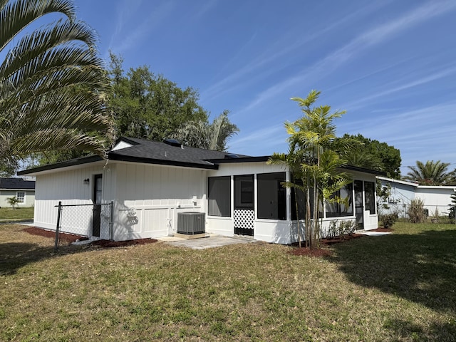 rear view of house with central air condition unit, a lawn, fence, and a sunroom