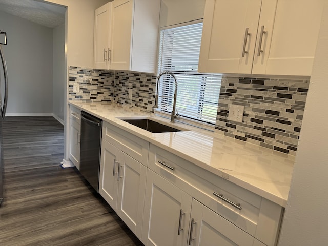 kitchen with a sink, dark wood finished floors, white cabinets, dishwashing machine, and light stone countertops