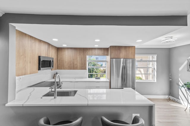 kitchen featuring brown cabinets, light stone counters, stainless steel appliances, a peninsula, and a breakfast bar area