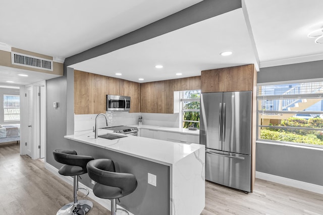 kitchen featuring visible vents, a kitchen bar, appliances with stainless steel finishes, brown cabinetry, and a sink