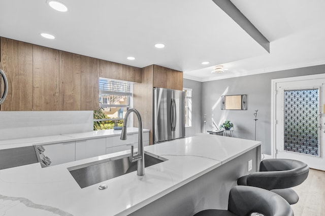 kitchen with brown cabinets, modern cabinets, a breakfast bar, a sink, and freestanding refrigerator