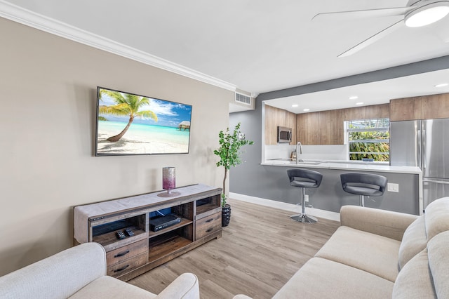 living area with a ceiling fan, baseboards, visible vents, light wood-style flooring, and crown molding