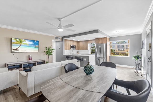 dining area with visible vents, baseboards, ceiling fan, ornamental molding, and light wood-style flooring