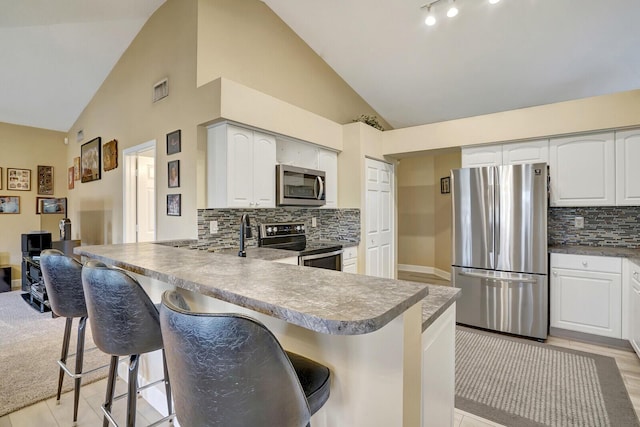 kitchen featuring stainless steel appliances, a peninsula, a breakfast bar area, white cabinets, and decorative backsplash