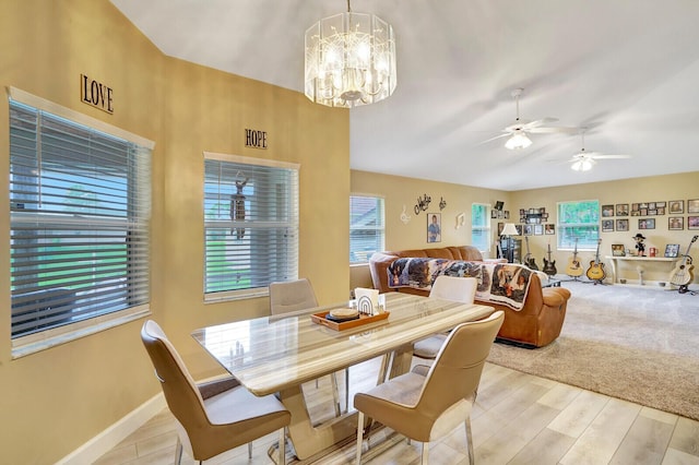 dining space with baseboards, light wood-style floors, vaulted ceiling, and ceiling fan with notable chandelier