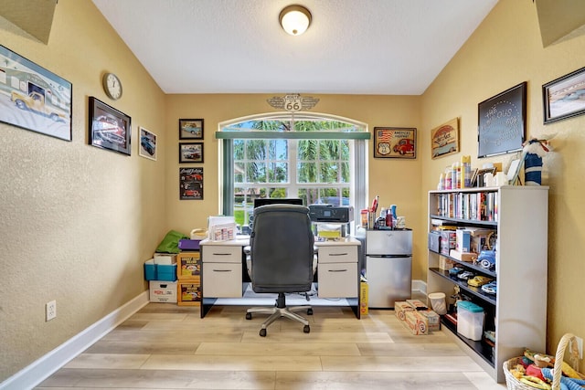 office space featuring a textured wall, baseboards, a textured ceiling, and light wood finished floors