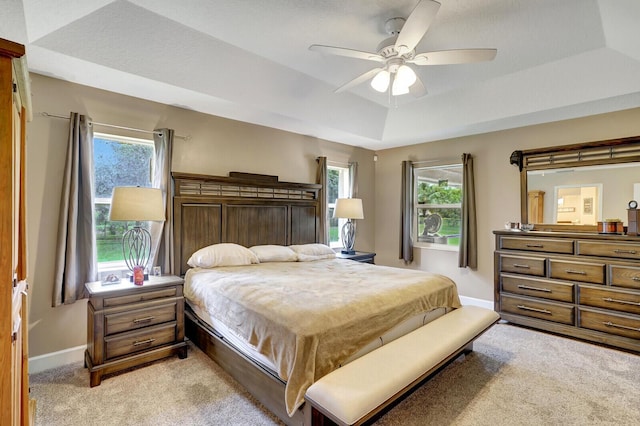 bedroom featuring a tray ceiling, multiple windows, light colored carpet, and baseboards