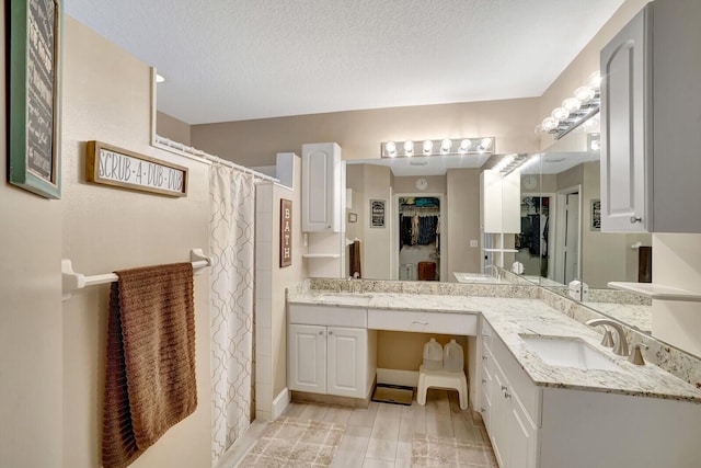 bathroom with double vanity, curtained shower, a textured ceiling, and a sink