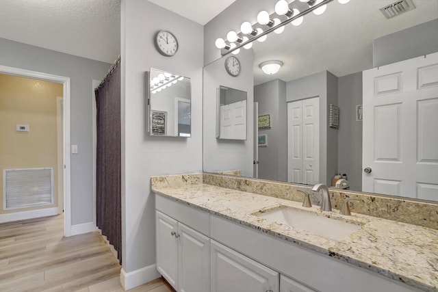 bathroom with vanity, wood finished floors, visible vents, and baseboards