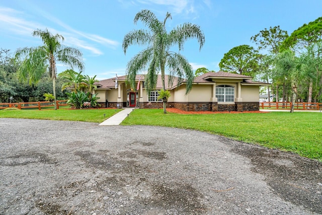 view of front of home featuring stucco siding, stone siding, a front yard, and fence