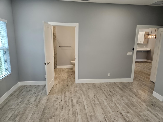 unfurnished bedroom with visible vents, baseboards, ensuite bathroom, light wood-type flooring, and a chandelier