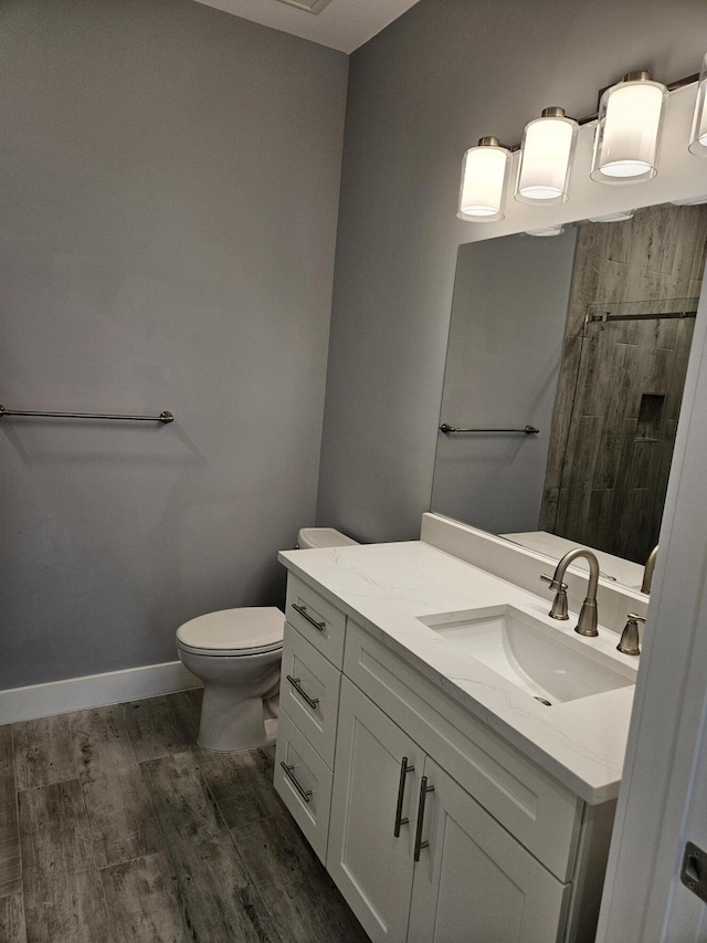 bathroom featuring toilet, wood finished floors, tiled shower, baseboards, and vanity