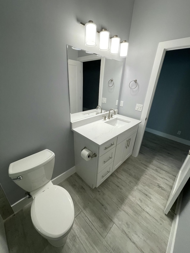 bathroom with baseboards, toilet, wood finished floors, and vanity