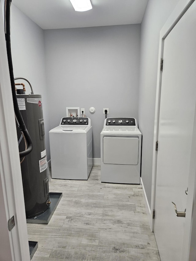 clothes washing area featuring baseboards, water heater, laundry area, wood finished floors, and separate washer and dryer