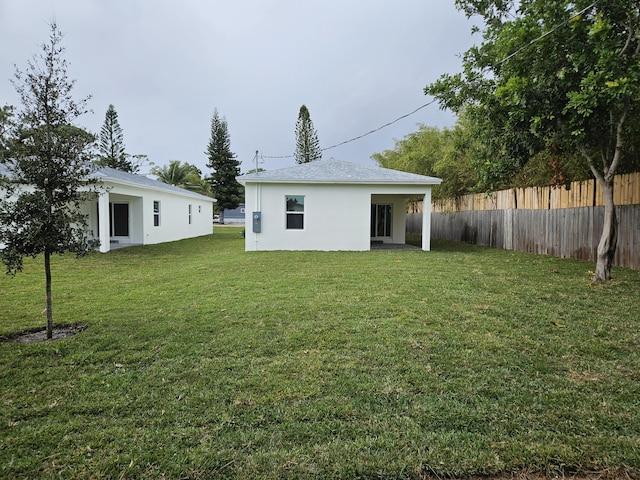 back of house with stucco siding, a yard, and fence