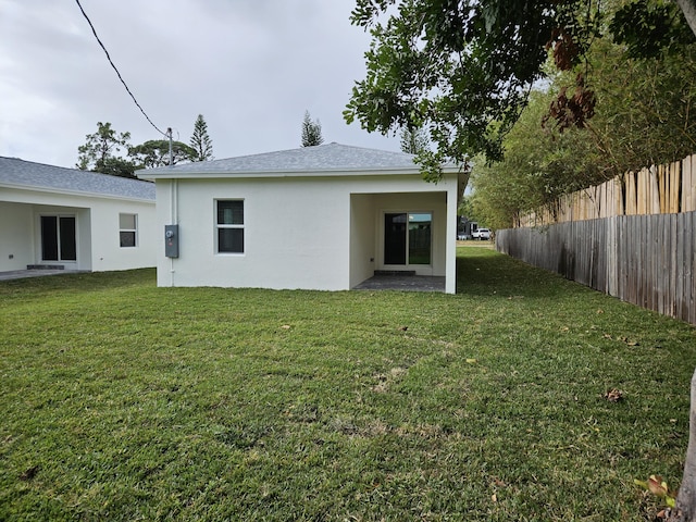 back of property with stucco siding, a lawn, and fence