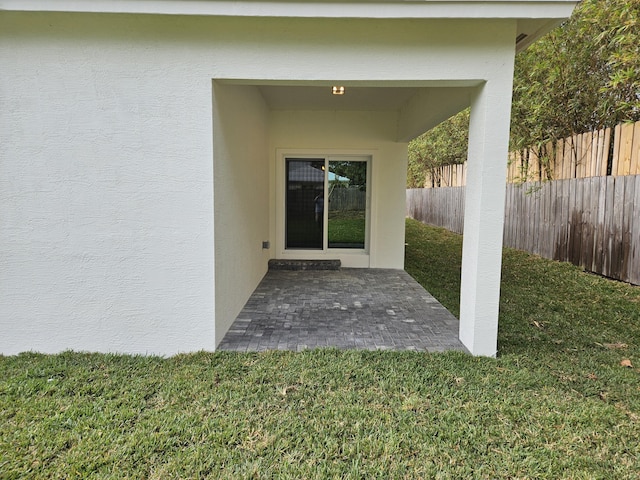 doorway to property with stucco siding, a patio, a lawn, and fence