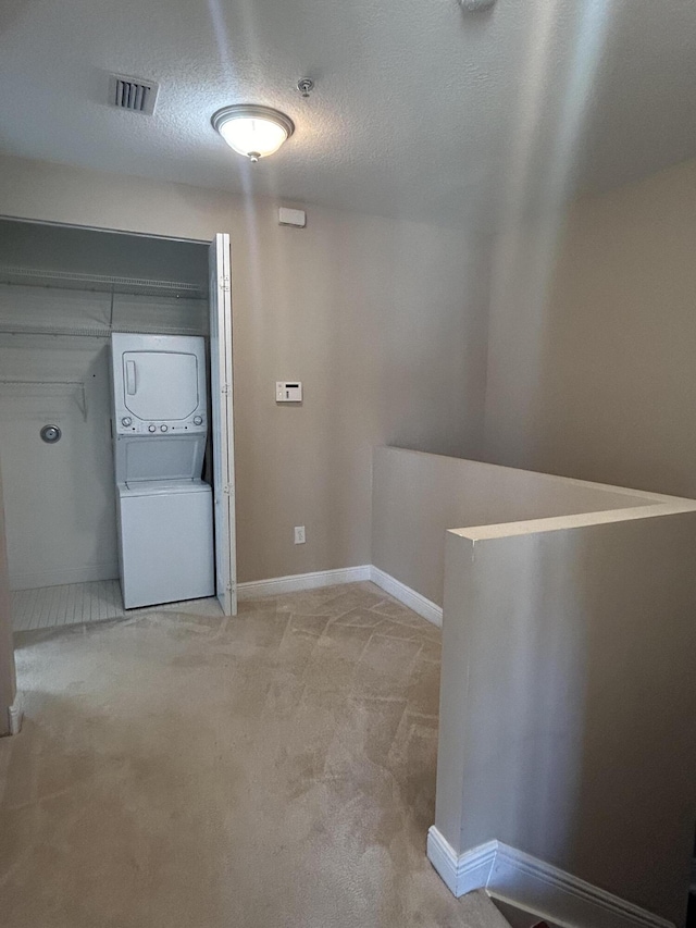 hall featuring visible vents, baseboards, light colored carpet, stacked washer and clothes dryer, and a textured ceiling