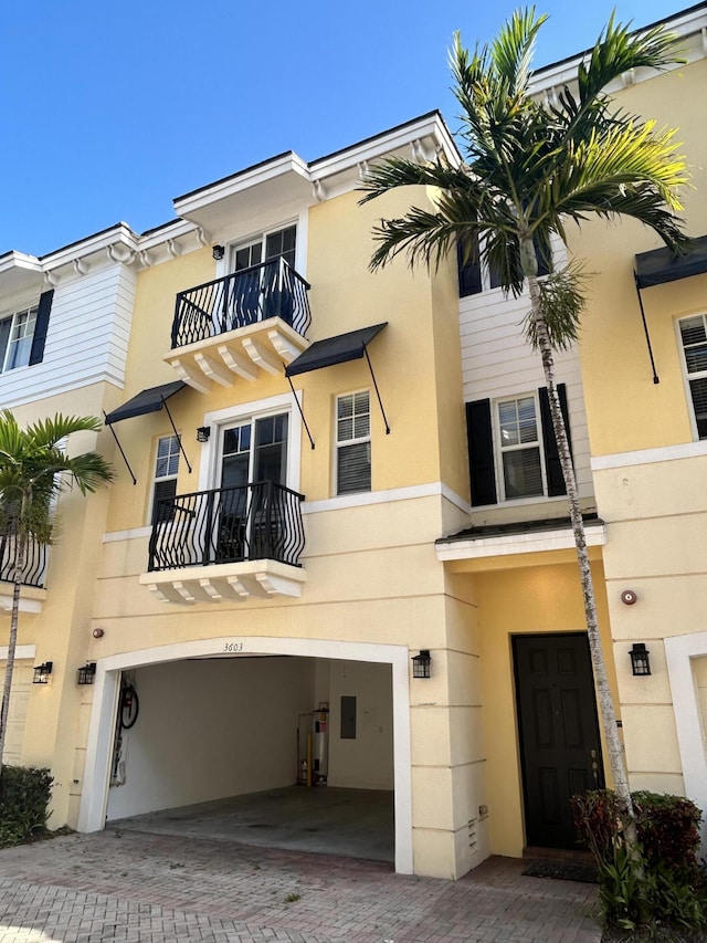 view of front facade featuring a balcony, stucco siding, decorative driveway, and a garage