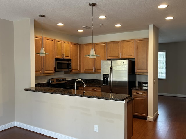 kitchen with dark wood-style floors, stainless steel appliances, dark stone counters, a peninsula, and brown cabinetry