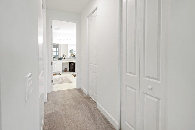 hallway featuring light colored carpet and baseboards