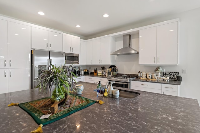 kitchen with dark stone countertops, white cabinetry, stainless steel appliances, and wall chimney range hood