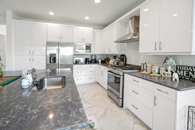 kitchen with marble finish floor, a sink, appliances with stainless steel finishes, white cabinets, and wall chimney range hood