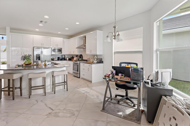 kitchen featuring visible vents, wall chimney range hood, a breakfast bar area, appliances with stainless steel finishes, and white cabinets