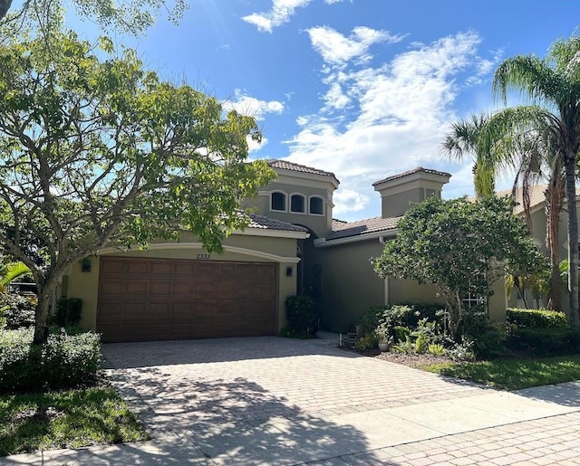 mediterranean / spanish house featuring a tiled roof, a garage, driveway, and stucco siding