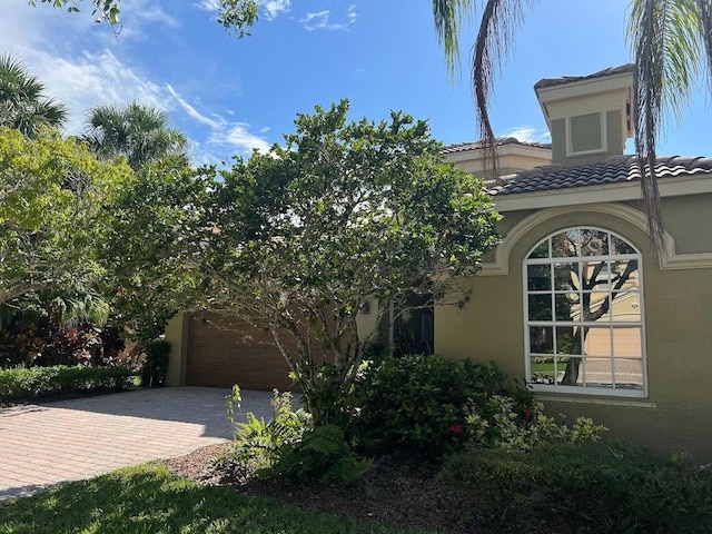 view of home's exterior with stucco siding, decorative driveway, an attached garage, and a tiled roof