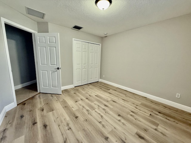 unfurnished bedroom featuring baseboards, visible vents, light wood finished floors, a closet, and a textured ceiling