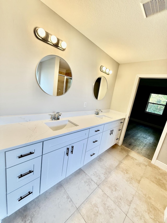 full bath featuring a textured ceiling, double vanity, visible vents, and a sink