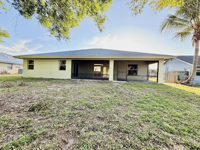 rear view of property featuring stucco siding, a lawn, and fence