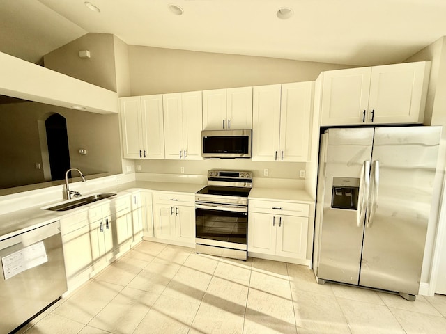 kitchen with a sink, stainless steel appliances, vaulted ceiling, white cabinets, and light countertops