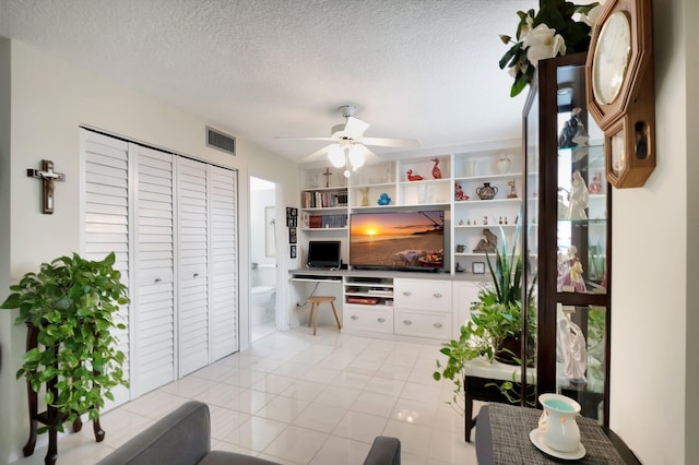 living area featuring light tile patterned floors, visible vents, a textured ceiling, and ceiling fan