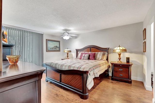 bedroom with ceiling fan, a textured ceiling, baseboards, and wood finished floors